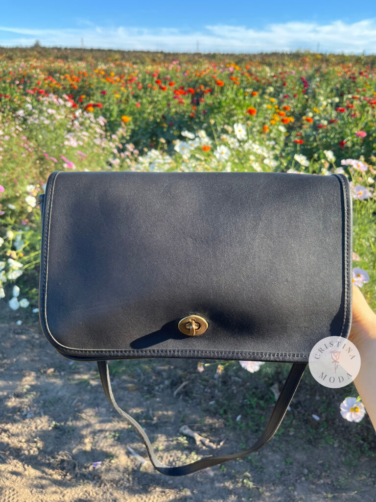 vintage coach convertible clutch held in front of a field of flowers